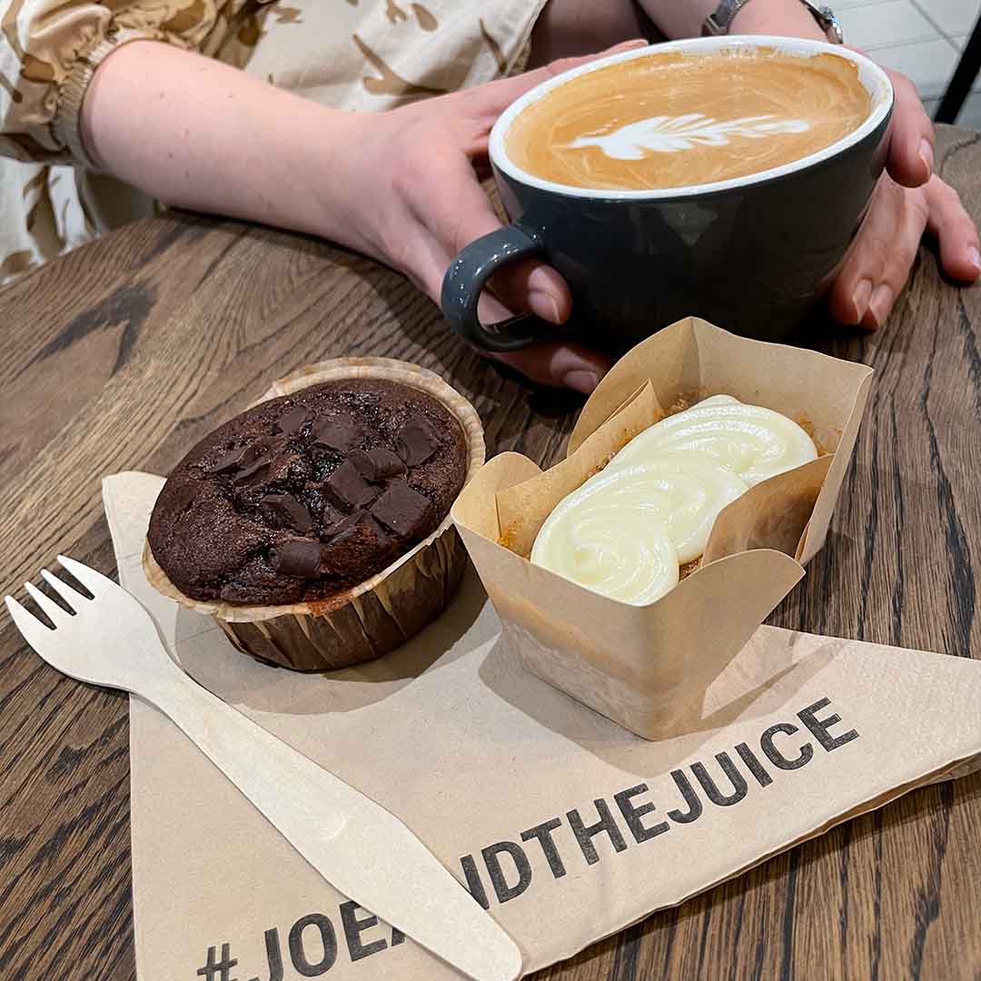 En kvinde nyder sin cappuccino og 2 små stykker kage på Joe & The Juice.  
